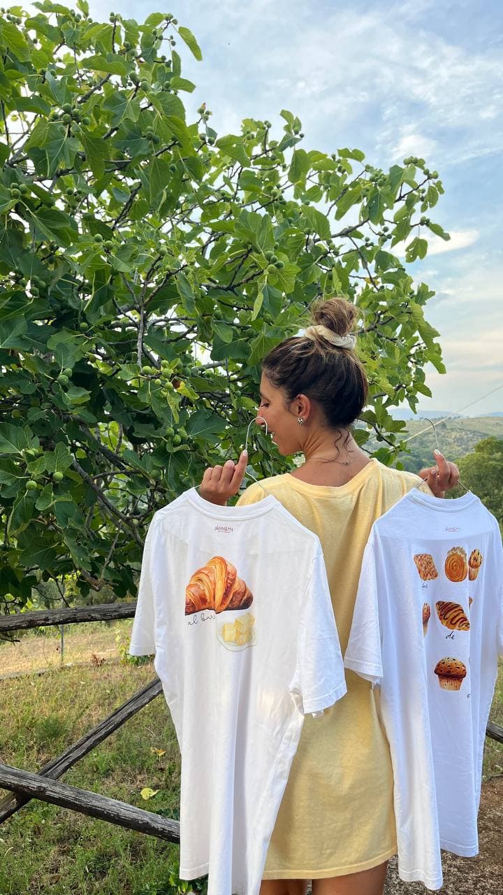 Michela Sharon regge due t-shirt Paneelatte di spalle tra gli alberi